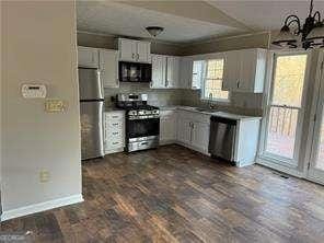 kitchen with a notable chandelier, baseboards, white cabinets, dark wood-type flooring, and stainless steel appliances