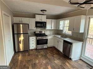 kitchen with dark wood-style flooring, light countertops, white cabinets, and stainless steel appliances