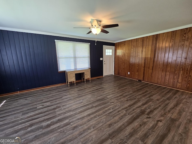 unfurnished living room featuring baseboards, wooden walls, dark wood-style floors, crown molding, and a ceiling fan