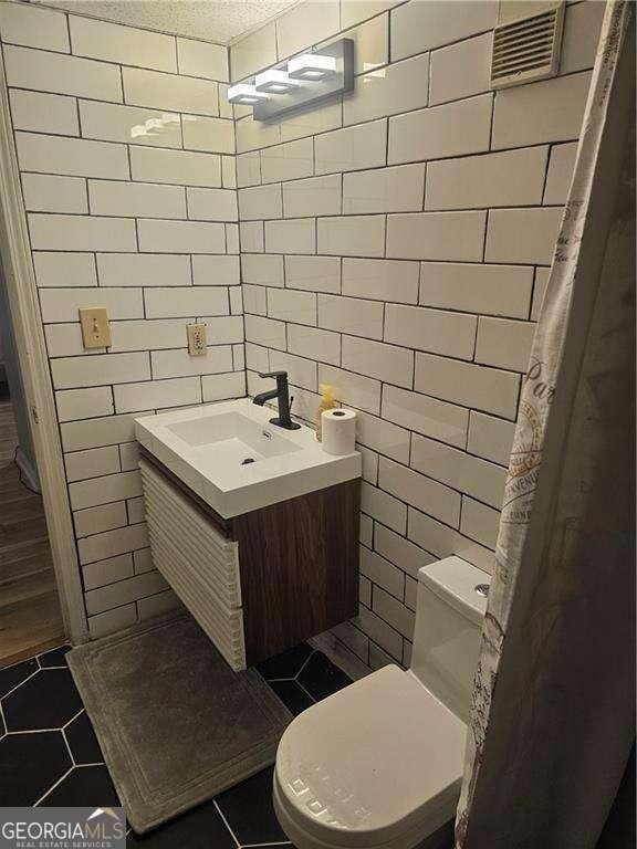 bathroom featuring tile patterned floors, visible vents, tile walls, and toilet