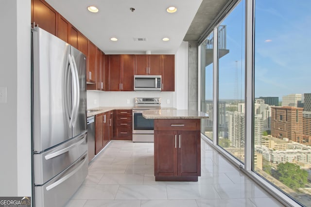 kitchen with tasteful backsplash, a kitchen island, light stone countertops, visible vents, and stainless steel appliances