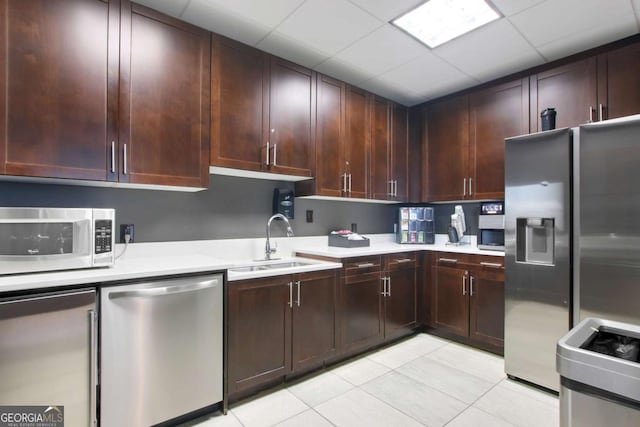 kitchen featuring light tile patterned floors, a sink, light countertops, a paneled ceiling, and stainless steel appliances