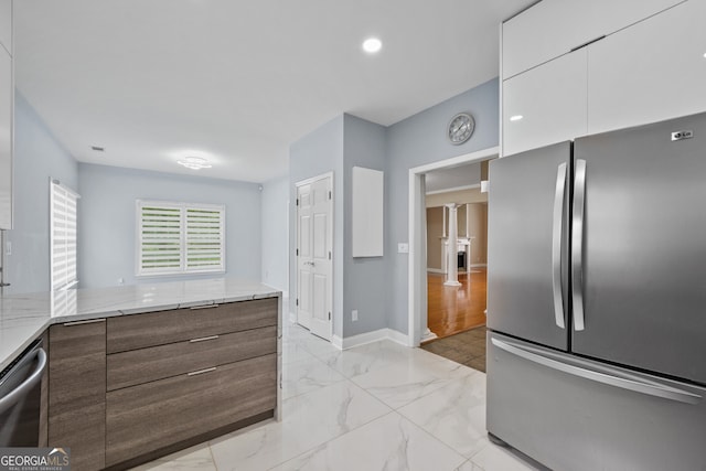 kitchen featuring stainless steel appliances, ornate columns, modern cabinets, and light stone countertops