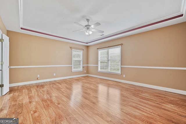 empty room with a tray ceiling, a ceiling fan, light wood-style floors, and baseboards