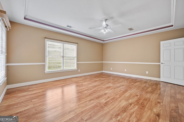 unfurnished room featuring a raised ceiling, a ceiling fan, light wood-style flooring, and baseboards