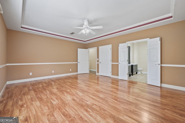 unfurnished bedroom featuring a raised ceiling, light wood finished floors, connected bathroom, and baseboards
