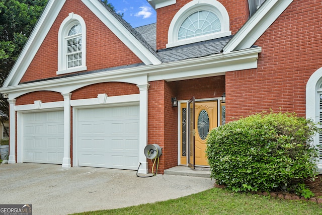 entrance to property featuring brick siding, concrete driveway, and a shingled roof