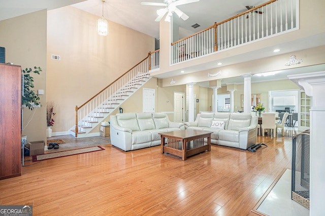 living area with a towering ceiling, ornate columns, stairway, a ceiling fan, and wood finished floors