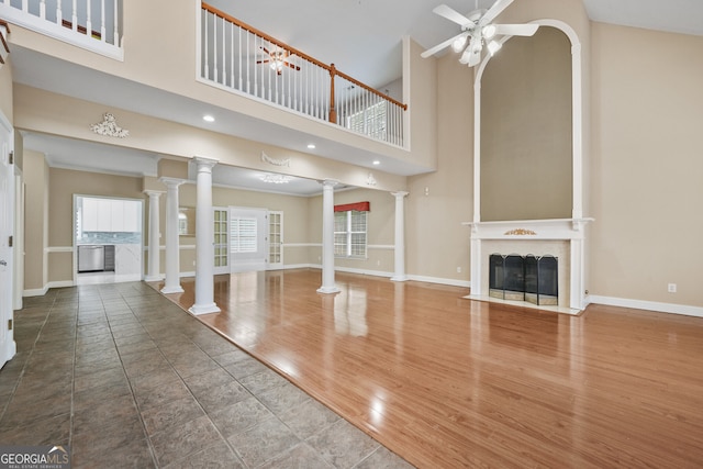 unfurnished living room with ornate columns, a high ceiling, baseboards, a ceiling fan, and a fireplace with flush hearth