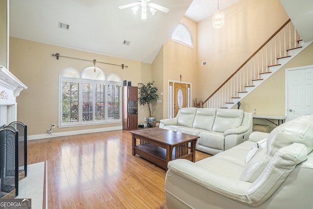 living area with high vaulted ceiling, light wood-style floors, stairs, ceiling fan, and baseboards