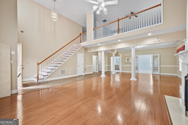 unfurnished living room featuring ornate columns, a towering ceiling, ceiling fan, wood finished floors, and a premium fireplace