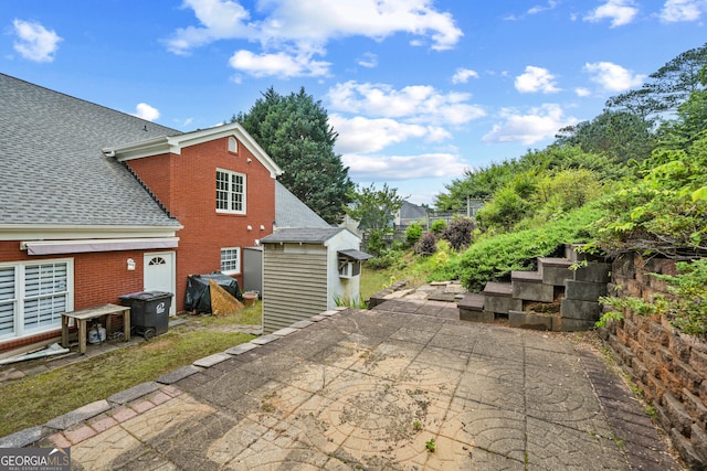back of house featuring a shingled roof, a patio area, brick siding, a storage shed, and an outdoor structure