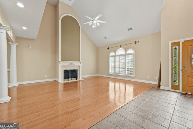 unfurnished living room with high vaulted ceiling, ceiling fan, decorative columns, a fireplace with flush hearth, and baseboards