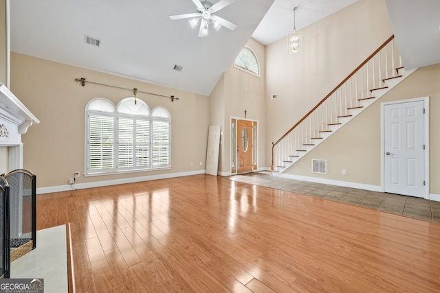 unfurnished living room featuring wood finished floors, high vaulted ceiling, ceiling fan, stairway, and a fireplace with flush hearth