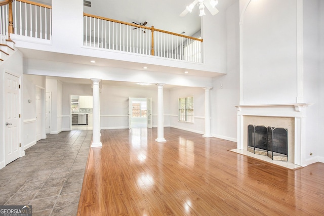 4505 Lakefield Bnd, Berkeley Lake, GA 30096 - unfurnished living room with decorative columns, a fireplace with flush hearth, a towering ceiling, ceiling fan, and wood finished floors