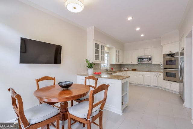 kitchen with appliances with stainless steel finishes, a peninsula, a sink, white cabinetry, and ornamental molding