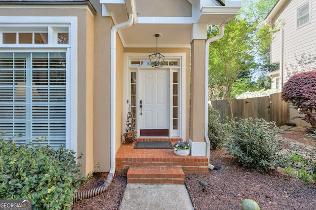 view of exterior entry featuring stucco siding and fence