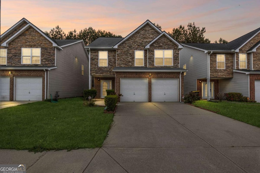 traditional-style home with stone siding, a front lawn, brick siding, an attached garage, and driveway