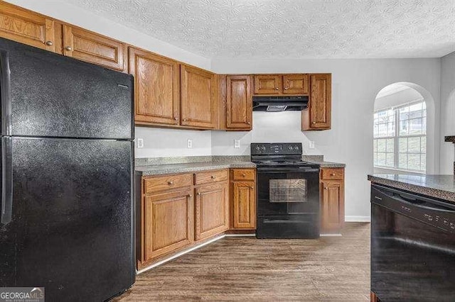 kitchen featuring dark wood-type flooring, under cabinet range hood, black appliances, and brown cabinetry