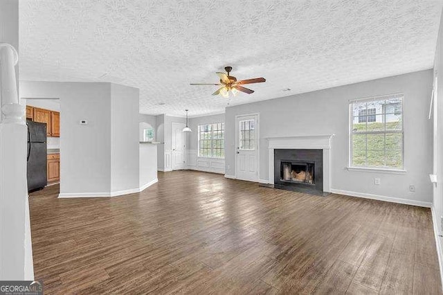 unfurnished living room with plenty of natural light, a fireplace with flush hearth, dark wood-style flooring, and ceiling fan