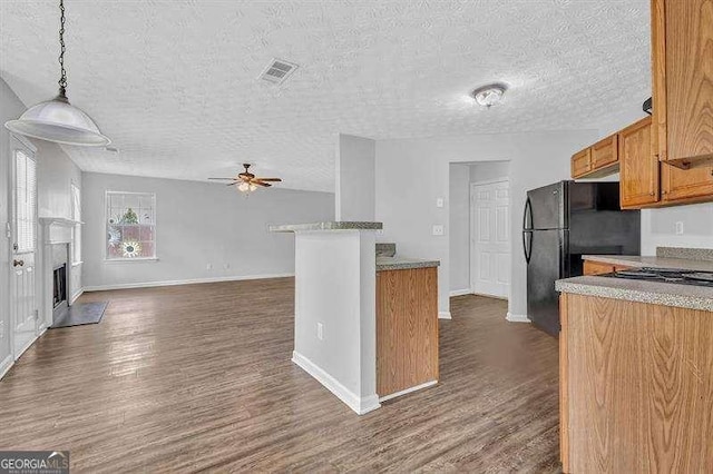 kitchen featuring visible vents, ceiling fan, a fireplace, brown cabinetry, and dark wood-type flooring