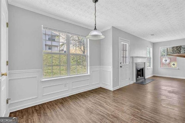 unfurnished dining area with a fireplace with raised hearth, wainscoting, wood finished floors, and a textured ceiling