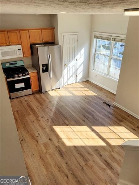 kitchen with light wood finished floors, visible vents, baseboards, a textured ceiling, and appliances with stainless steel finishes