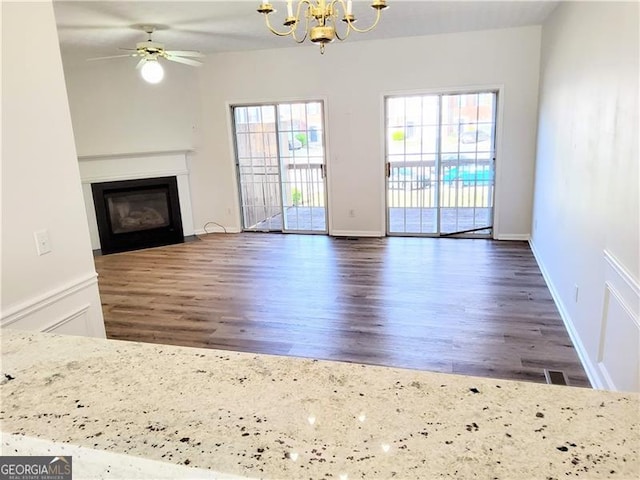 unfurnished living room with a glass covered fireplace, wood finished floors, and ceiling fan with notable chandelier