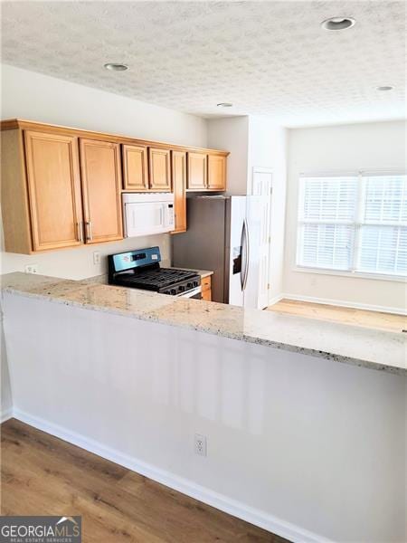 kitchen with recessed lighting, wood finished floors, light stone countertops, baseboards, and appliances with stainless steel finishes