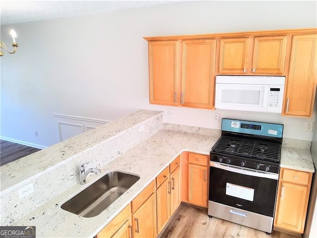 kitchen with light wood-type flooring, white microwave, stainless steel gas range oven, and a sink