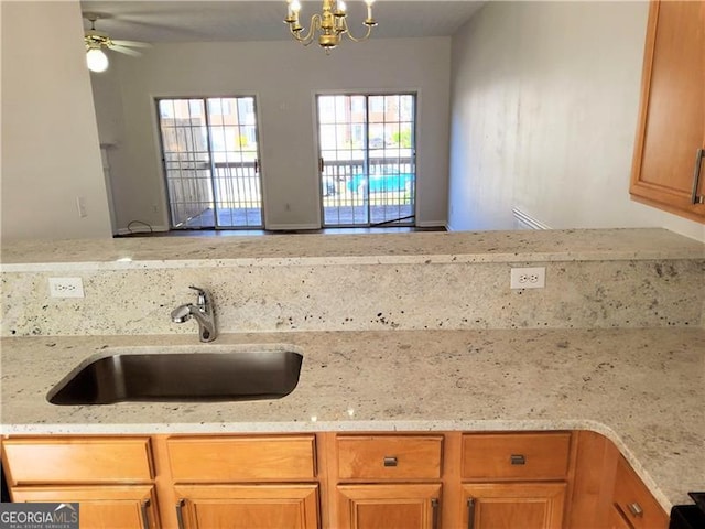 kitchen featuring a sink, open floor plan, ceiling fan with notable chandelier, light stone countertops, and brown cabinetry