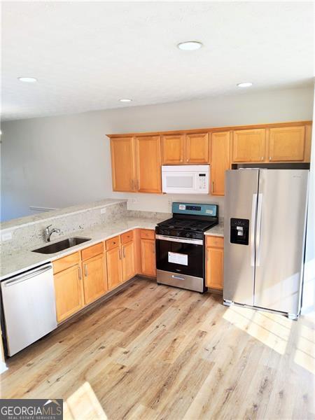 kitchen featuring light countertops, light wood finished floors, appliances with stainless steel finishes, and a sink