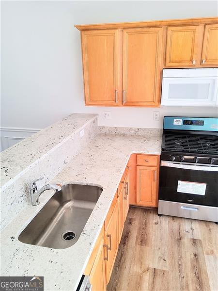 kitchen with light stone counters, a sink, light wood finished floors, white microwave, and stainless steel gas range oven