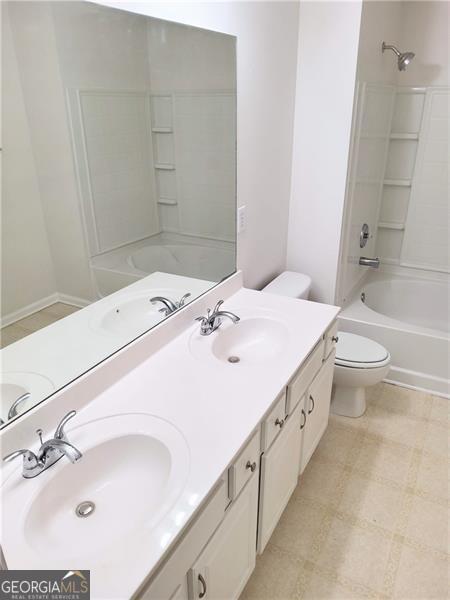 full bath with shower / washtub combination, double vanity, toilet, and a sink
