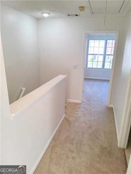 hall with an upstairs landing, attic access, light colored carpet, baseboards, and visible vents