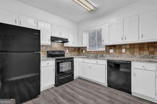 kitchen with white cabinets, a textured ceiling, under cabinet range hood, black appliances, and wood finished floors