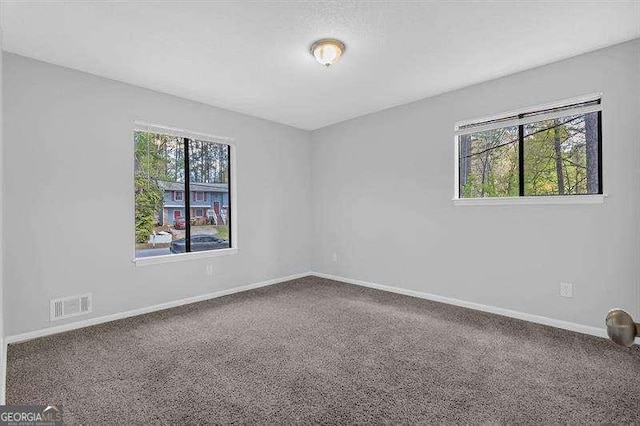 carpeted empty room featuring baseboards, visible vents, and a wealth of natural light