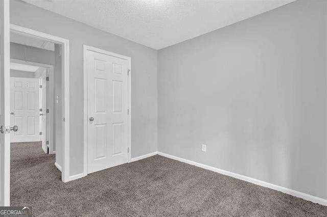 unfurnished bedroom featuring dark colored carpet, a textured ceiling, and baseboards