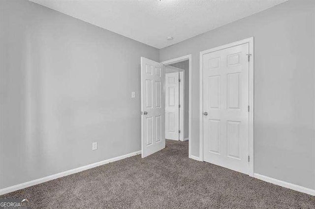 unfurnished bedroom featuring dark colored carpet, baseboards, and a textured ceiling
