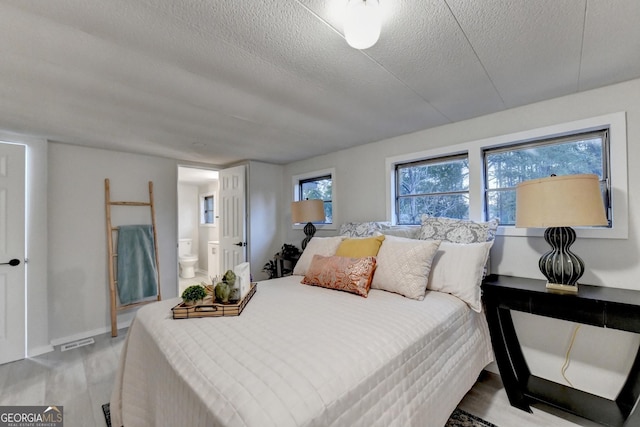 21 W Lake Dr, Oxford, GA 30054 - bedroom with connected bathroom, a textured ceiling, visible vents, wood finished floors, and baseboards
