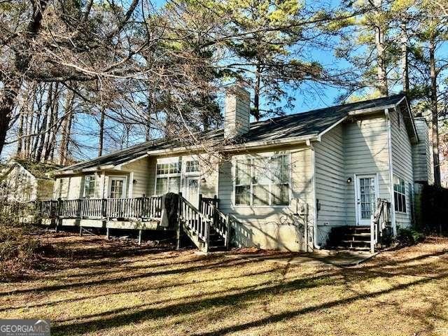 back of property with entry steps, a chimney, a deck, and a lawn
