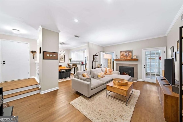 living room featuring crown molding, wood finished floors, a tiled fireplace, and baseboards