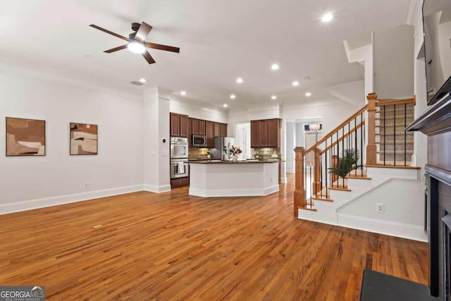 unfurnished living room featuring baseboards, ornamental molding, ceiling fan, light wood-type flooring, and stairway