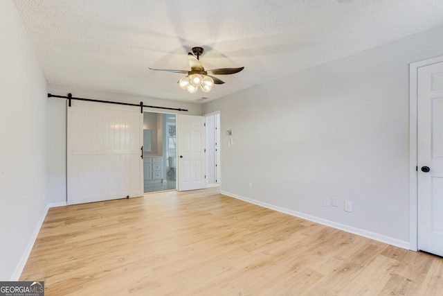 5465 N Fork Dr SW, Lilburn, GA 30047 - unfurnished bedroom with baseboards, light wood-type flooring, a barn door, and a textured ceiling