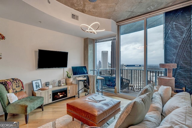 living room featuring expansive windows, a notable chandelier, light wood-type flooring, a lit fireplace, and visible vents