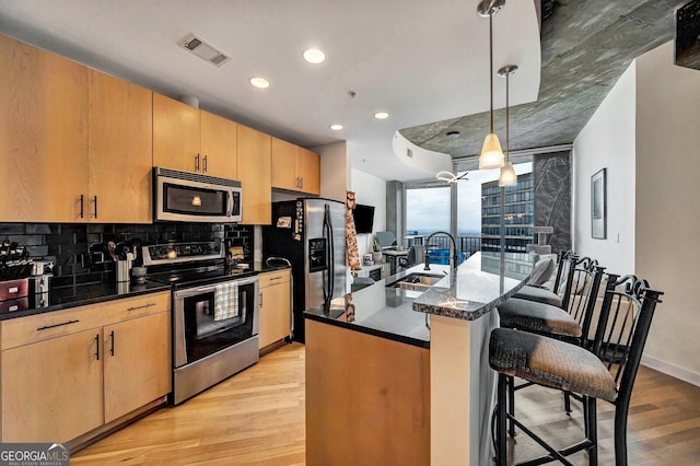 kitchen featuring light wood-style flooring, a sink, a breakfast bar, stainless steel appliances, and decorative backsplash