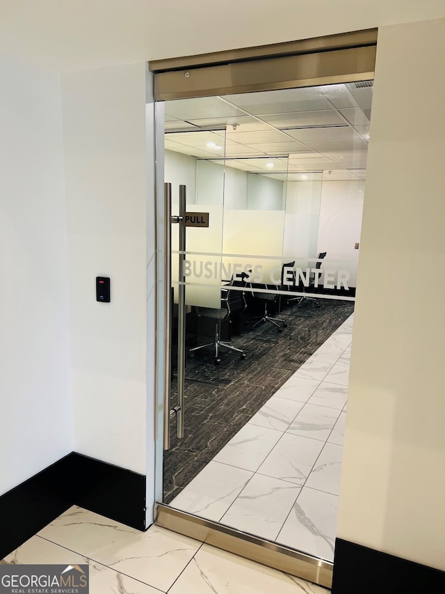 interior space with marble finish floor, baseboards, and a drop ceiling