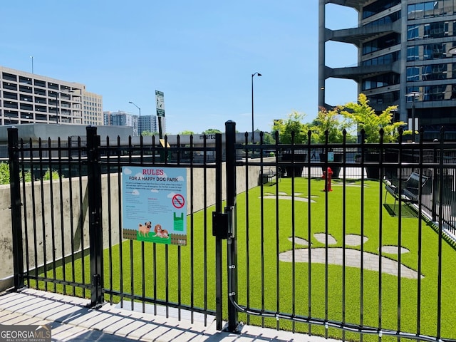 view of gate featuring fence, a lawn, and a city view