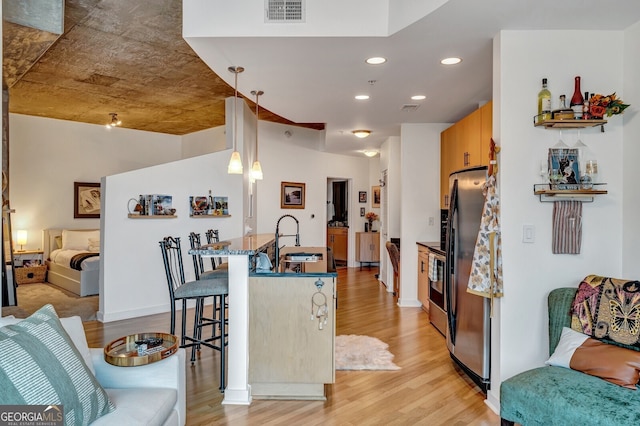 kitchen with a breakfast bar, freestanding refrigerator, visible vents, light wood finished floors, and a sink