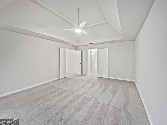 unfurnished bedroom featuring a tray ceiling, carpet flooring, baseboards, and ceiling fan